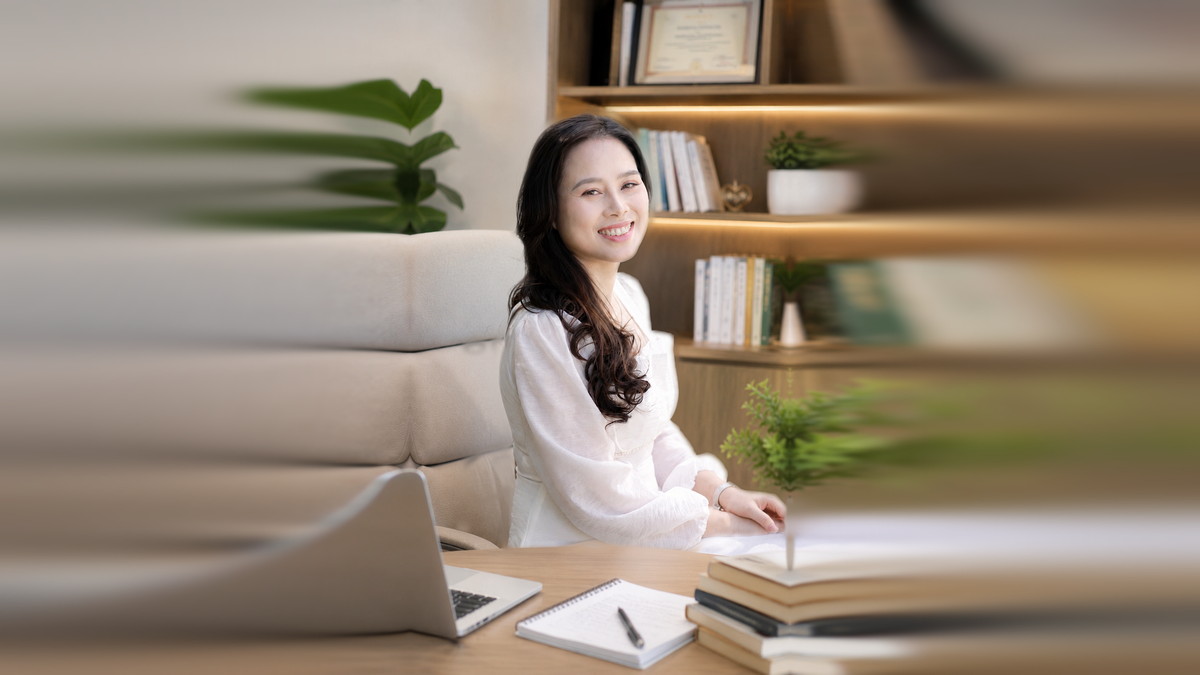 Nguyễn Tú Oanh ngồi bên bàn làm việc có máy tính, nơi tôi làm việc với anh chị qua Zoom